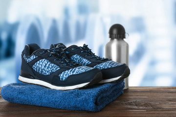 Canvas Print - Sport shoes, towel and bottle on table against blurred gym interior background