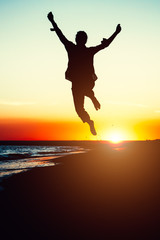 Silhouette young woman jumping with hands up on the beach at the sunset. Travel photo summertime