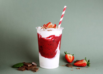 Wall Mural - Delicious strawberry dessert with cream and chocolate in plastic cup on green background