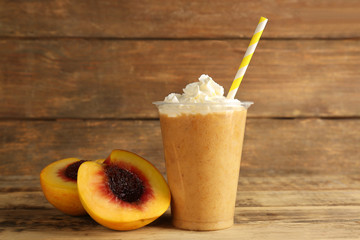 Wall Mural - Tasty peach milkshake with cream in plastic cup on wooden background
