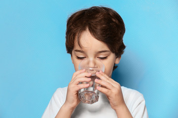 Cute little boy drinking water from glass on blue background