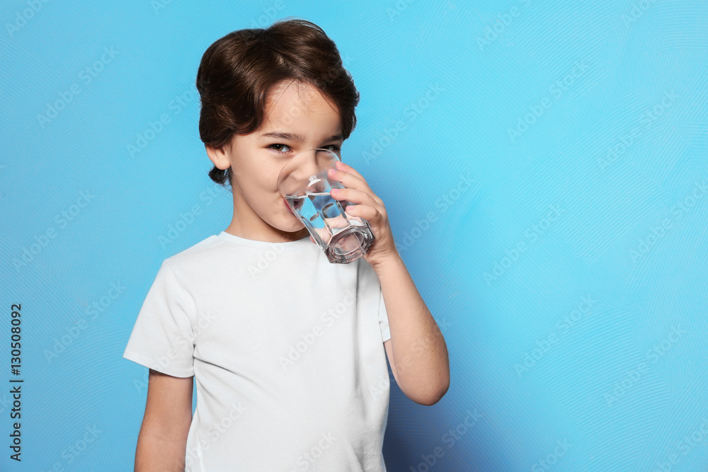 Cute little boy drinking water from glass on blue background