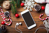 Fototapeta Desenie - Smart phone mock up with headphones and rustic Christmas decorations for app presentation. View from above