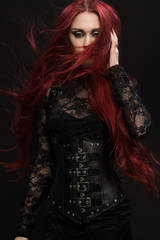 Young woman with red hair in black gothic costume on dark background