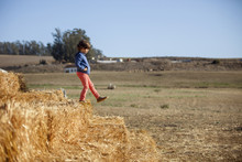 Side View Of Boy Walking Down Heap Of Hay Bales At Farm