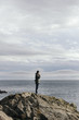 © Cavan Images - Side view of man standing on rock formation by sea against cloudy sky