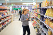 © lado2016 - Woman shopping in supermarket reading product information.Using smarthone