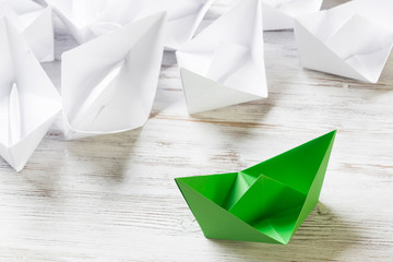 Business leadership concept with white and color paper boats on wooden table