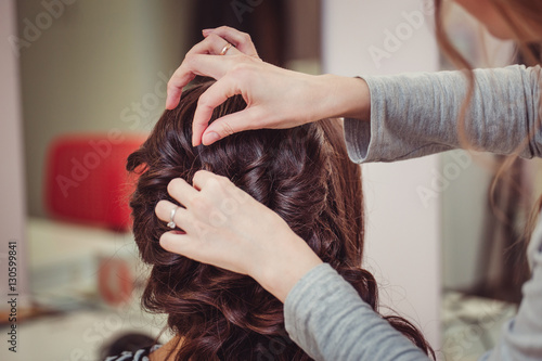 Fotografija Stylist curling hair and making wedding hairstyle for brown haired woman