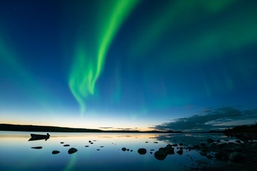 aurora at dusk - bands of curvy aurora borealis appear over a northern rocky lake right after sunset