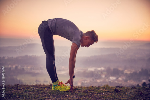 Fotografía Ragazzo fa stretching al parco in cima alla collina con vista sulla città