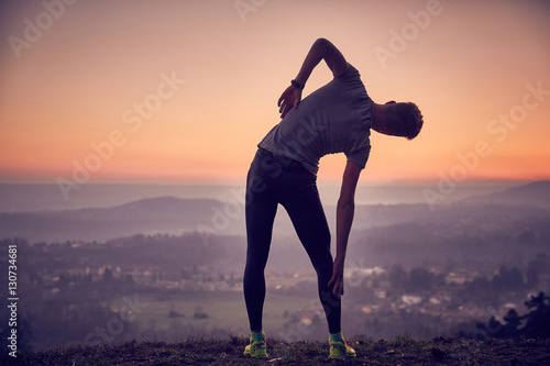 Fotomural Ragazzo fa stretching al parco in cima alla collina con vista sulla città