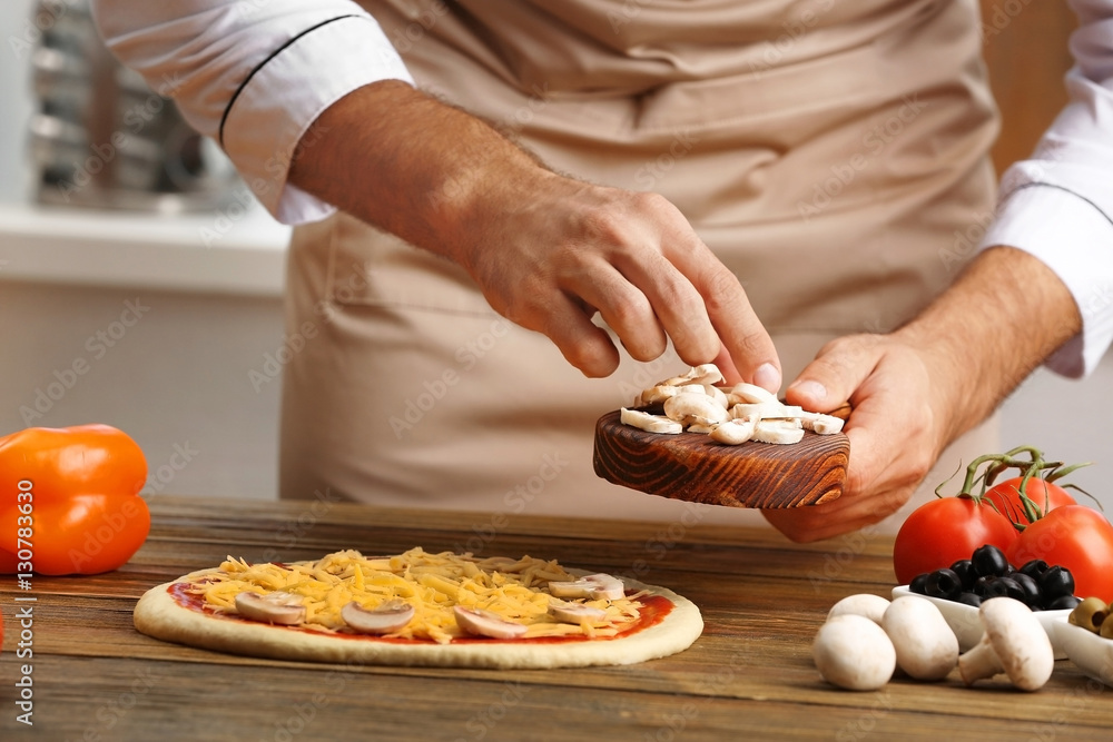 Male hands preparing pizza at wooden table closeup
