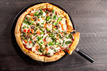 Home made pizza from scratch topped with mushrooms, turkey, kale, peppers, and tomatoes cut on a dark background