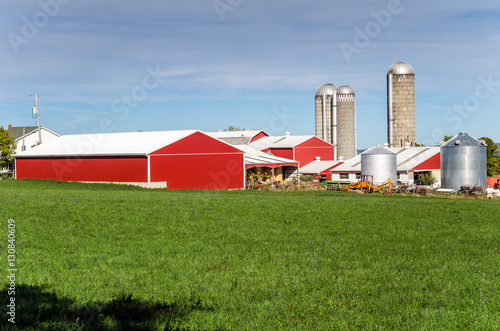 Farm With Red Barns And Silos With A Grassy Field In Foreground