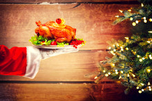 Christmas Holiday Dinner. Santa's Hand Holding Roasted Chicken Over Wooden Background