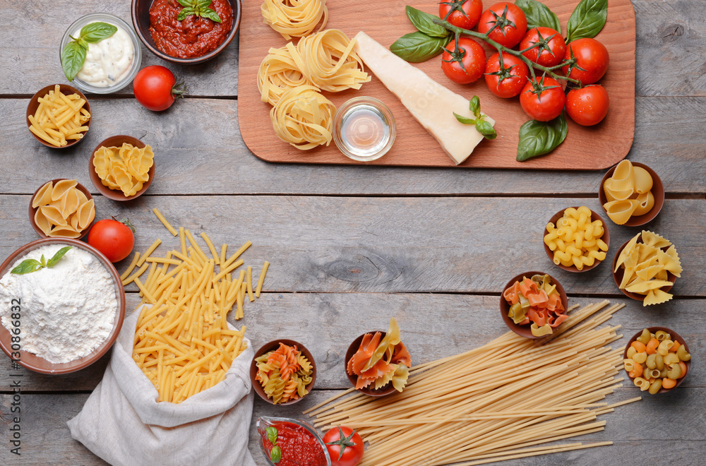 Different kinds of pasta and tomatoes on wooden background