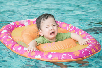 Closeup a baby boy sit in a boat for children in the swimming pool background in fear emotion