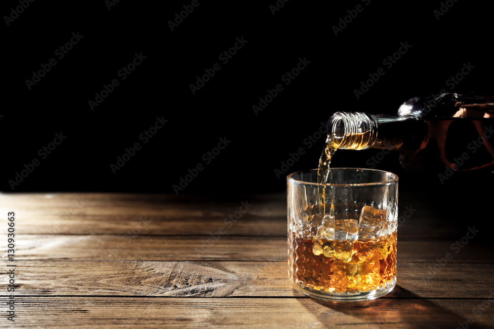 Pouring whisky into glass on wooden table closeup - obrazy, fototapety, plakaty 