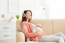 Young Pregnant Woman Listening To Music And Sitting On Sofa In The Room