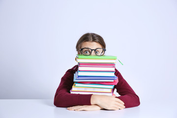 Poster - Teenage girl with pile of books sitting at table on white background