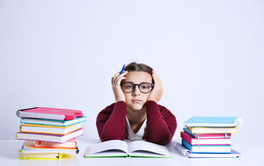 Poster - Teenage girl with pile of books sitting at table on white background