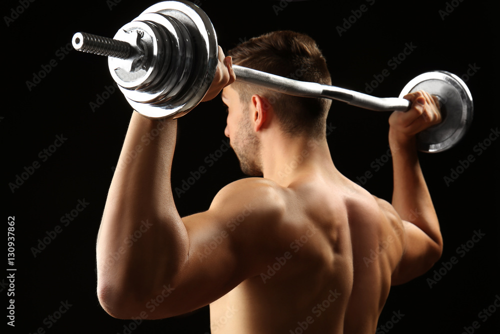 Sporty man doing exercises with barbell on black background