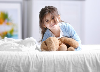 Wall Mural - Funny little girl lying on bed with cuddly toy