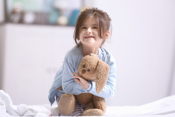 Wall Mural - Funny little girl sitting on bed with cuddly toy