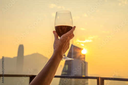 Photo Close up of glass of red wine raised with the background the spectacular Hong Kong skyline at sunset