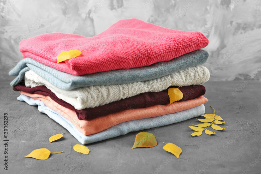 Stack of folded clothes with autumn leaves on grey background