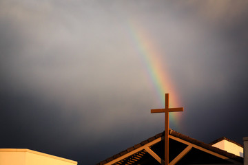 A passing storm creates a rainbow over this church cross.