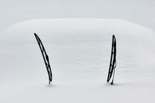 Two Windscreen Wipers Poking Out Of A Blanket Of Snow Covering A Car