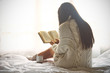 Young woman sitting in bed while reading a book