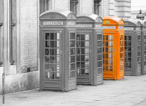Fototapeta na wymiar Five Red London Telephone boxes all in a row, in black and white with one booth in orange