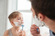 Father and son shaving in bathroom looking at each other