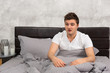 © kolotype - Young man woke up and sitting in stylish bed in grey colors