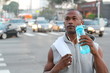 © ajr_images - African American Sport man drinking water bottle in New York City. Male runner sweaty and thirsty after run in the busy city street with traffic