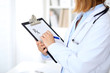 © rogerphoto - Close up of  female doctor  writing a medical prescription at clipboard while standing
