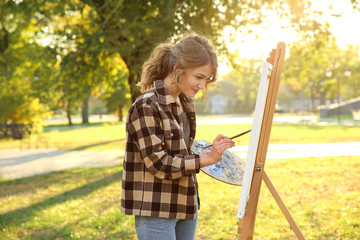 Young female artist painting picture in autumn park