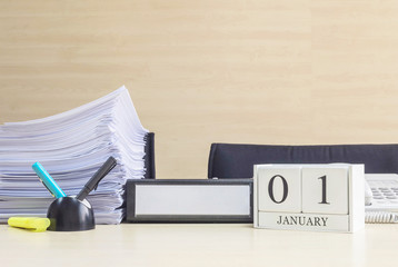 Closeup white wooden calendar with black 1 january word on blurred brown wood desk and wood wall textured background in office room view with copy space , selective focus at the calendar