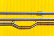 Metal horizontal pipes and tray on the wall of an industrial building of yellow vertical sandwich panels. Front view.