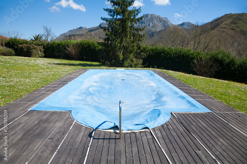 Plakat basen z drewnianą krawężnik zamknięty i pokryty niebieską plandeką na wiosnę Zielona łąka zaokrąglona górami w Przyrodzie w Asturii w Hiszpanii w Europie