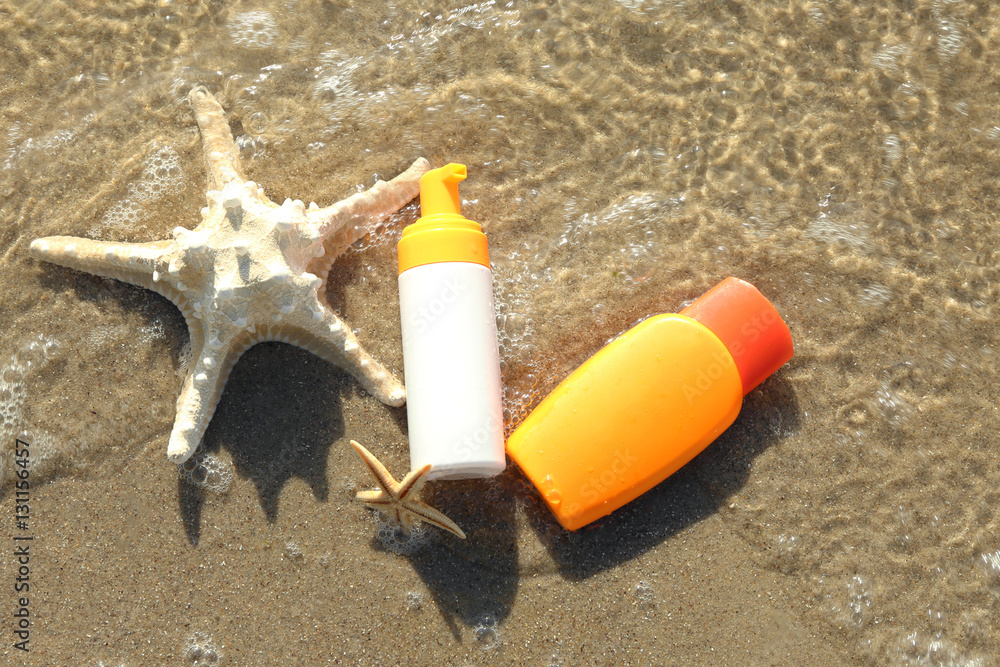 Lotion bottles with starfishes on beach sand