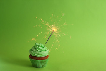 Fresh tasty cupcake with sparkler on green background