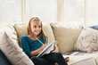 © Connect Images - Girl sitting on sofa writing in notebook