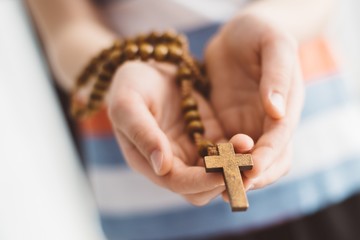 Little boy child praying and holding wooden rosary.