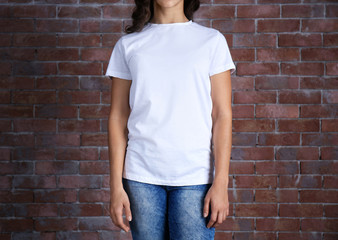 Wall Mural - Young woman in blank white t-shirt standing against brick wall, close up