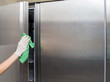 Hand in protective glove with rag cleaning kitchen equipment in the professional kitchen. Stainless steel refrigerator. Early spring cleaning or regular clean up.