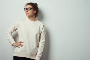 Portrait of charming woman hipster wearing blank sweater and eye glasses. White grunge wall with cracks background
